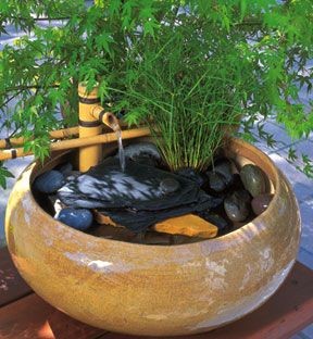 A stone bowl designed with stones, vigorously growing aquatic plants, 
and flowing water from a bamboo fountain.
