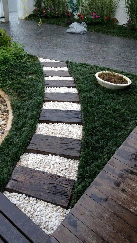 A small but eye-catching garden pathway where the white pebbles and dark-brown wooden planks stand out between the two patches of deep green grass.