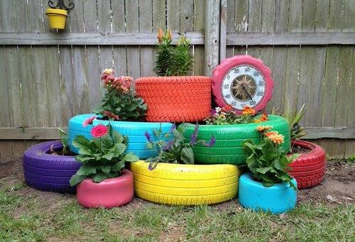Old tires used as raised garden beds next to a fence.